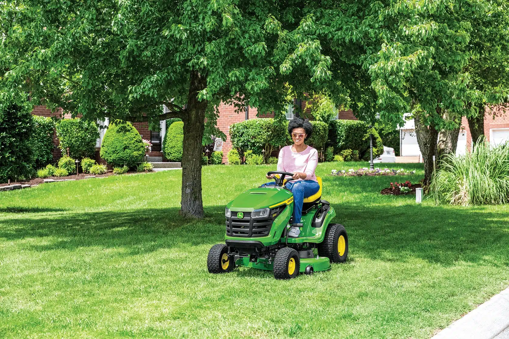 John Deere riding mower cutting grass on a large lawn.